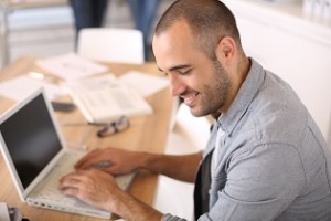 Smiling young man in office working on laptop