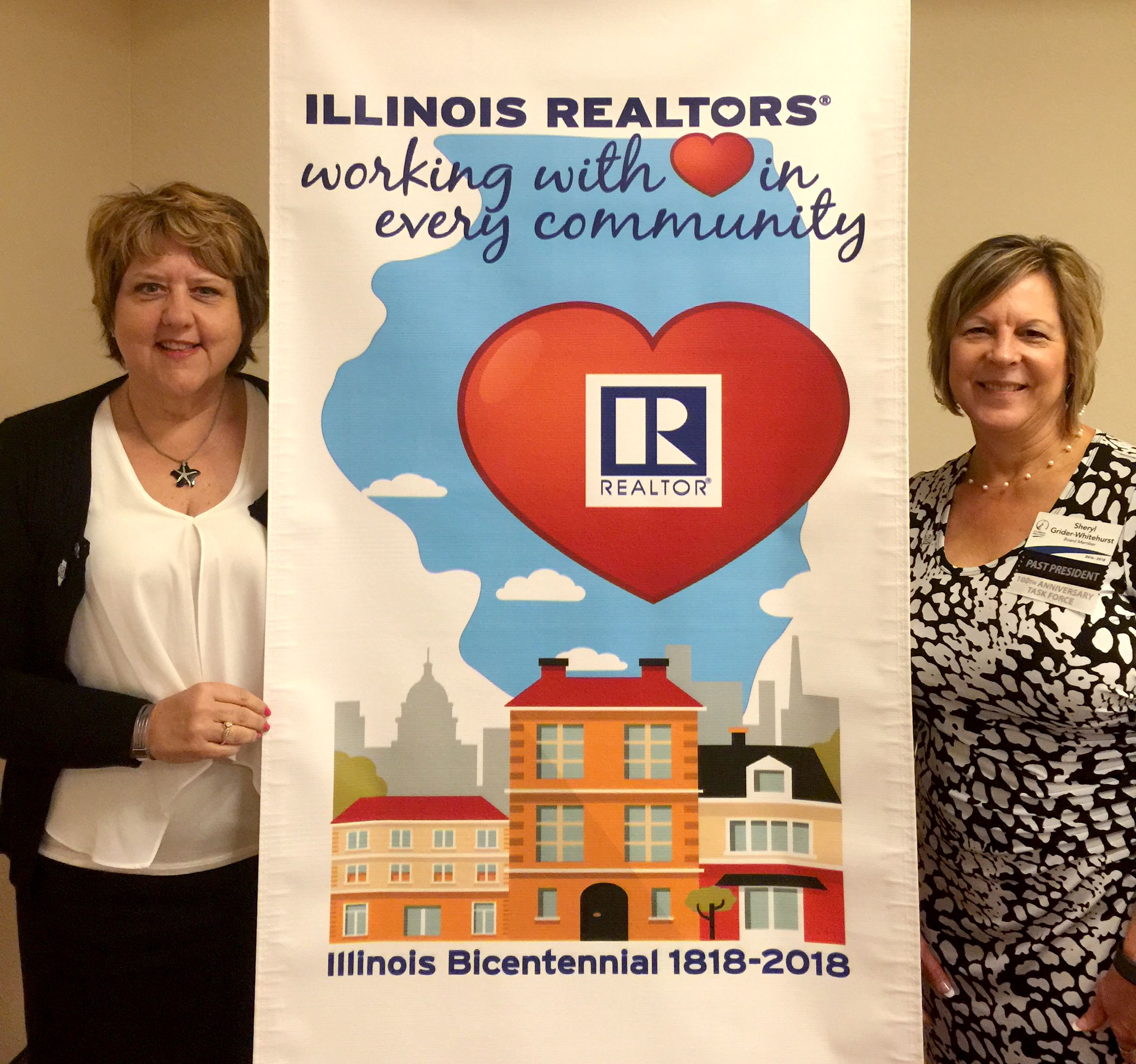 Illinois REALTORS® Bicentennial Task Force Chair Vicky Turner and Vice Chair Sheryl Grider Whitehurst pose with the logo designed to commemorate the association's recognition of the state's 200th birthday in 2018.