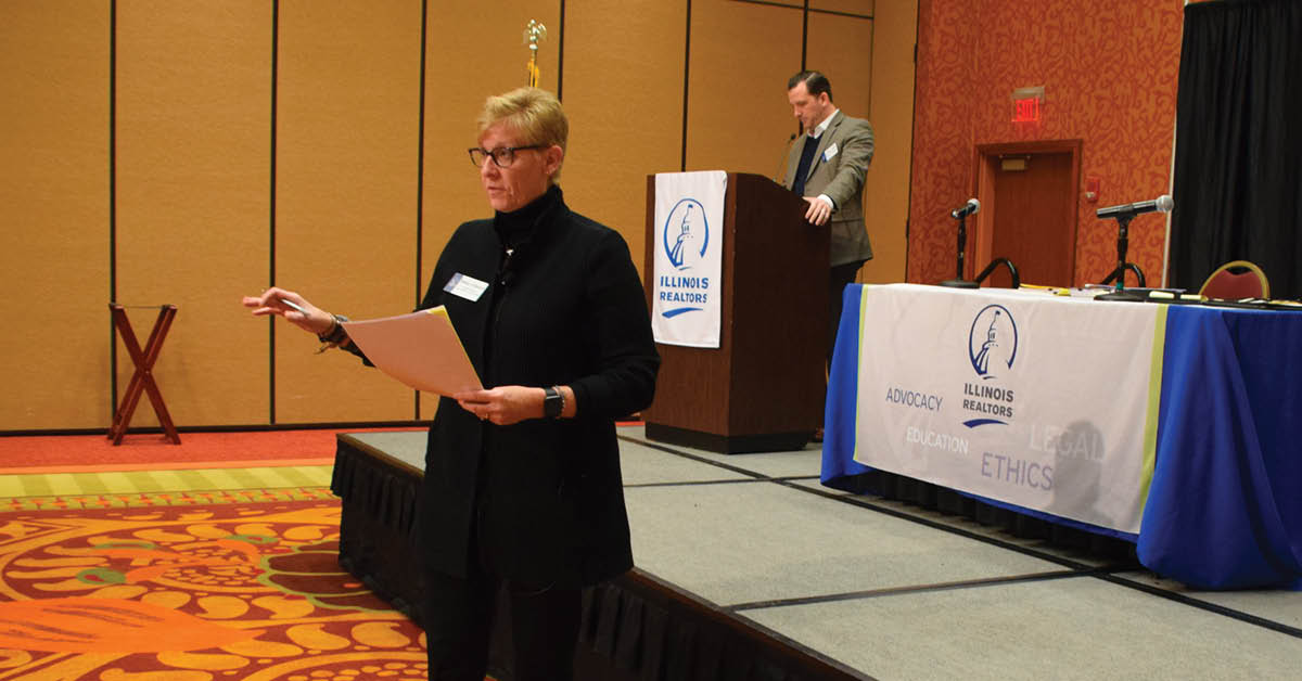 Betsy Urbance talks from in front of the stage while Jeffrey T. Baker is at the podium.