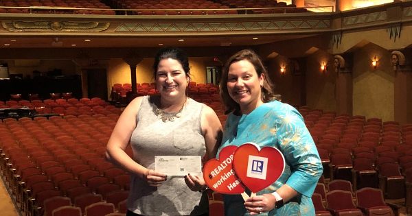Photo of an Egyptian Theatre representative holding a check from HomeTown REALTORS®, inside the Egyptian Theatre with Immediate Past President Alison Rosenow.