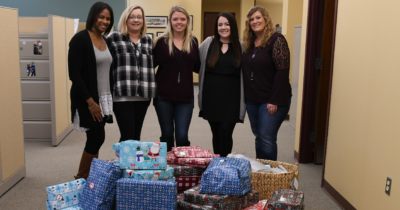 Five staff members stand behind a stack of presents.