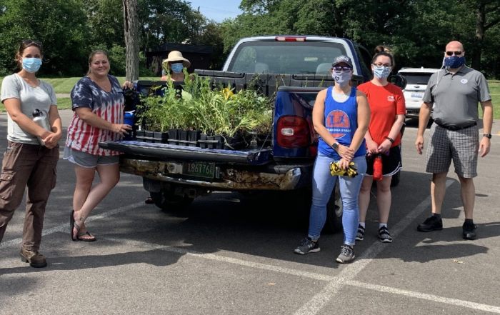 Six volunteers stand around pickup truck full of new plants